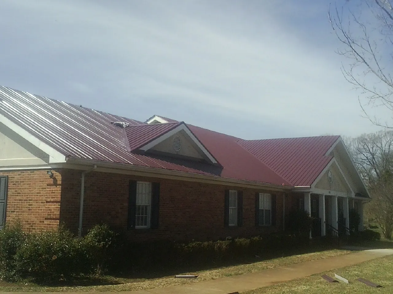 Red metal roof with gabled entries on a long brick building, from a Hail Damage Roof Repair job in Whiting