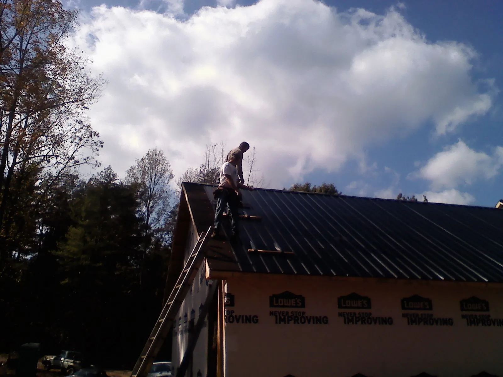 Roofer fastening dark metal panels high against a cloudy sky, from a Roof Inspection job in Whiting