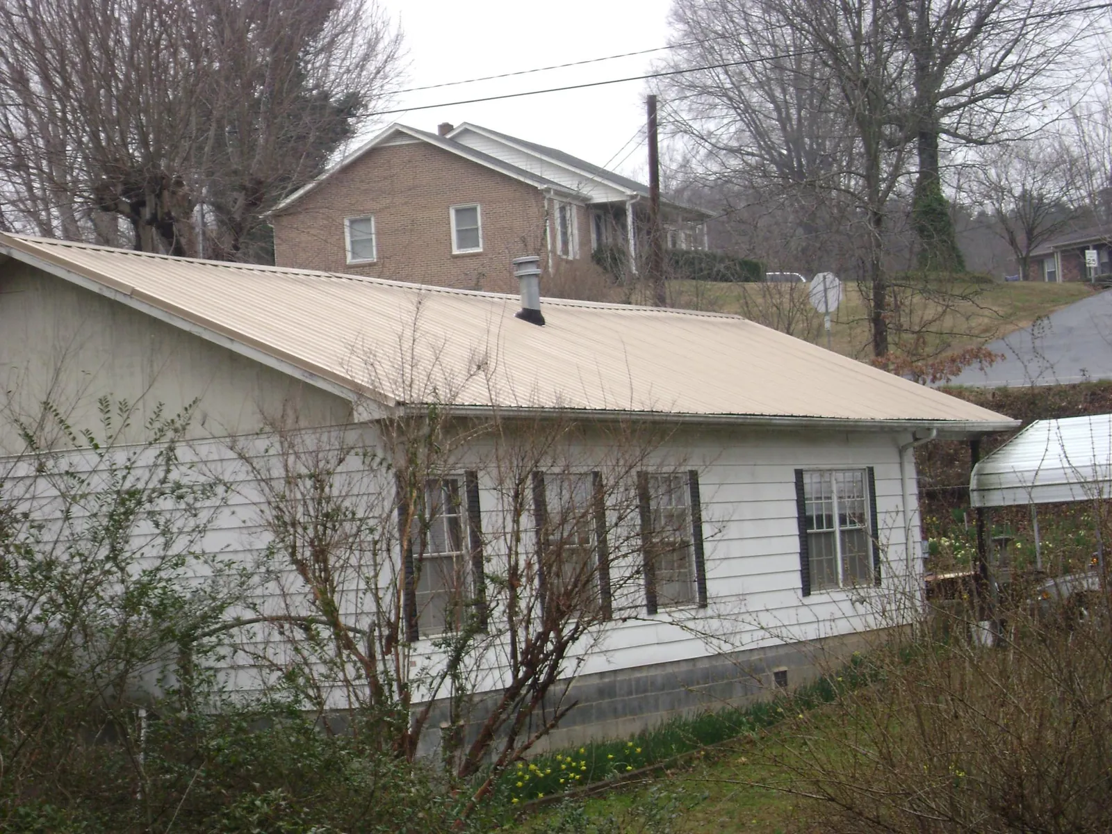 Tan metal roof on a white sided house set into a hillside — Commercial Roofing by Roofing Brothers in Whiting